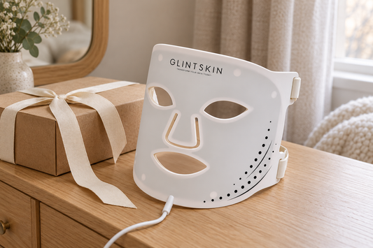White GlintSkin LED face mask beside a wrapped kraft gift box on a wooden dressing table